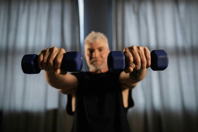 An older man lifting light dumbbells at home